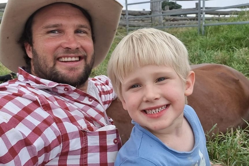 A man in a red checkered shirt smiles next to a young boy with blonde hair in a paddock A man in a red checkered shirt smiles next to a young boy with blonde hair in a paddock