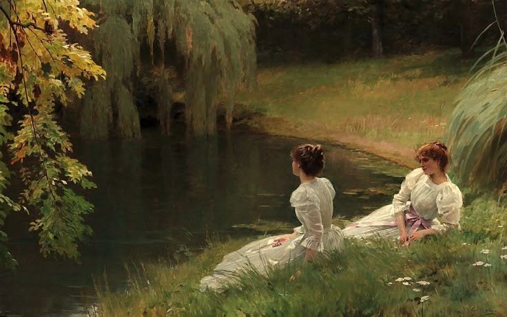 This may contain: two women in white dresses sitting on the grass by a pond with trees and water behind them