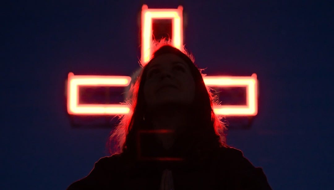 a woman standing in front of a lighted cross a woman standing in front of a lighted cross
