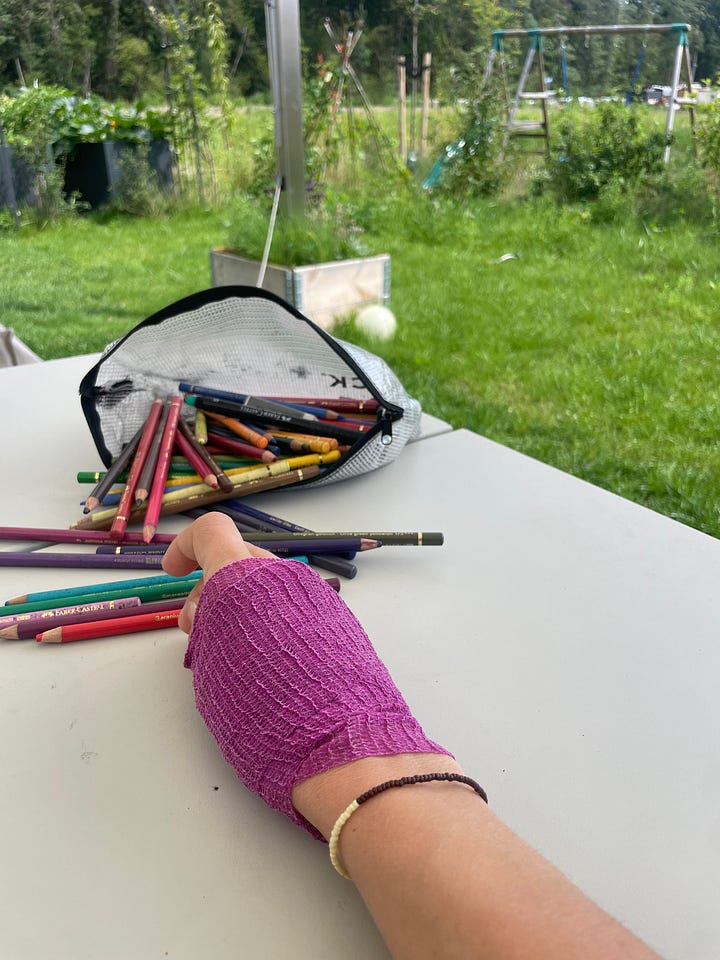 A hand wrapped in a bright purple bandage rests on a white table next to scattered colored pencils spilling from a mesh bag, with a lush green garden visible in the background & A soft colored pencil self-portrait drawn with non-dominant hand, showing a seated figure in pink and green tones with gentle, uncertain lines