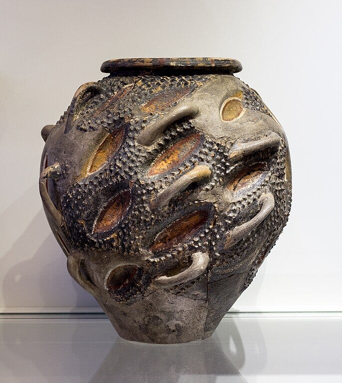 Minoan pithos (storage jar) painted black, red, yellow, and white, with 3D bumps, hollows, and looped handles all over it.