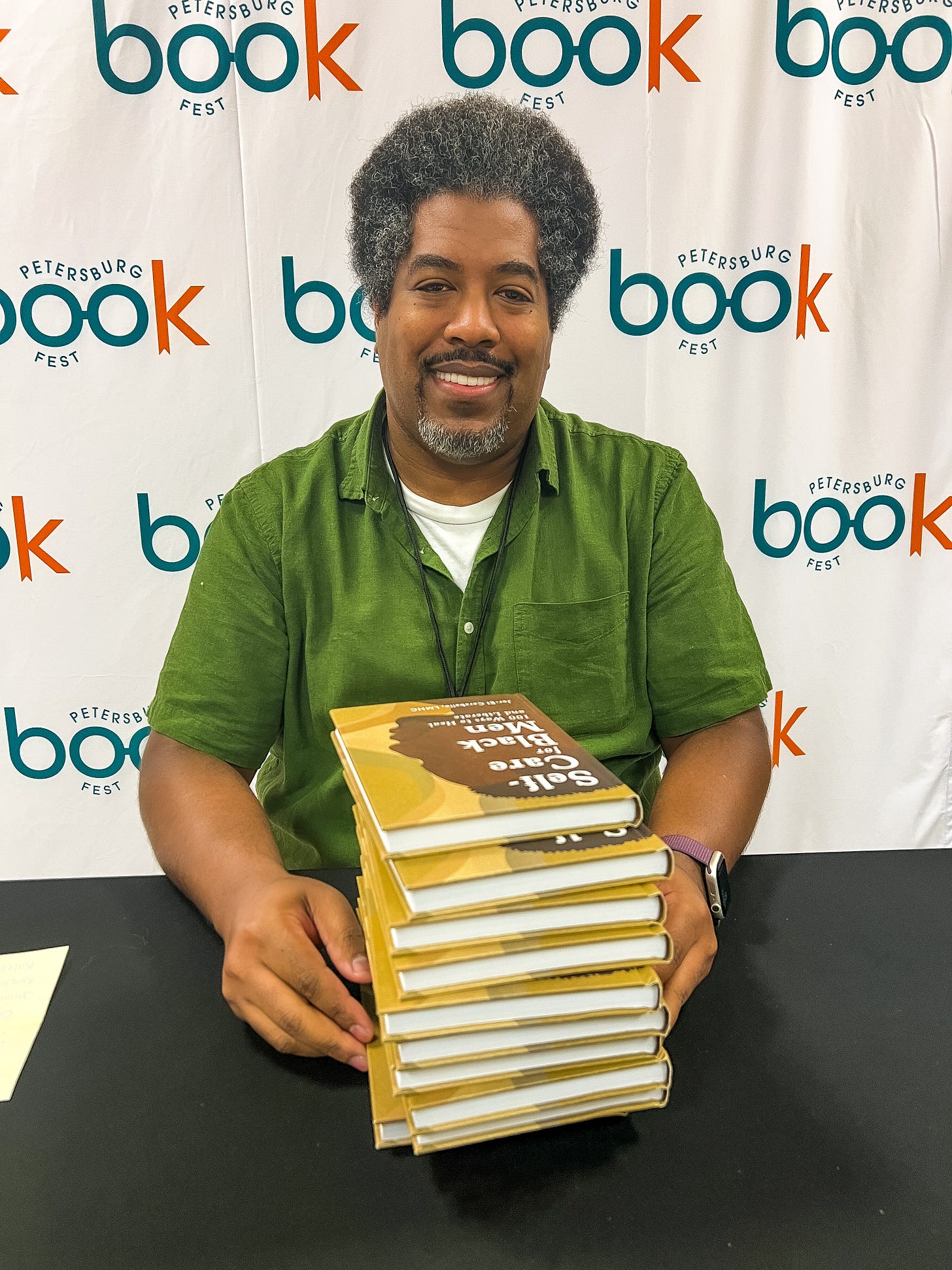 Jor-El Caraballo author of Self-Care for Black Men at the Petersburg Book Fest holding a stack of books