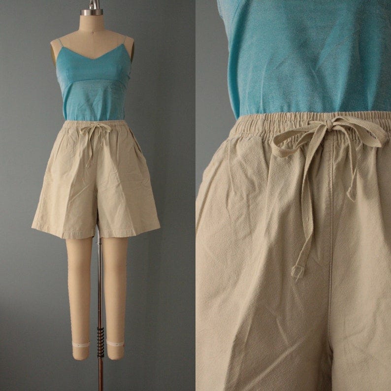 May include: Beige cotton shorts with a drawstring waist. The shorts have a relaxed fit and are a versatile piece of clothing.