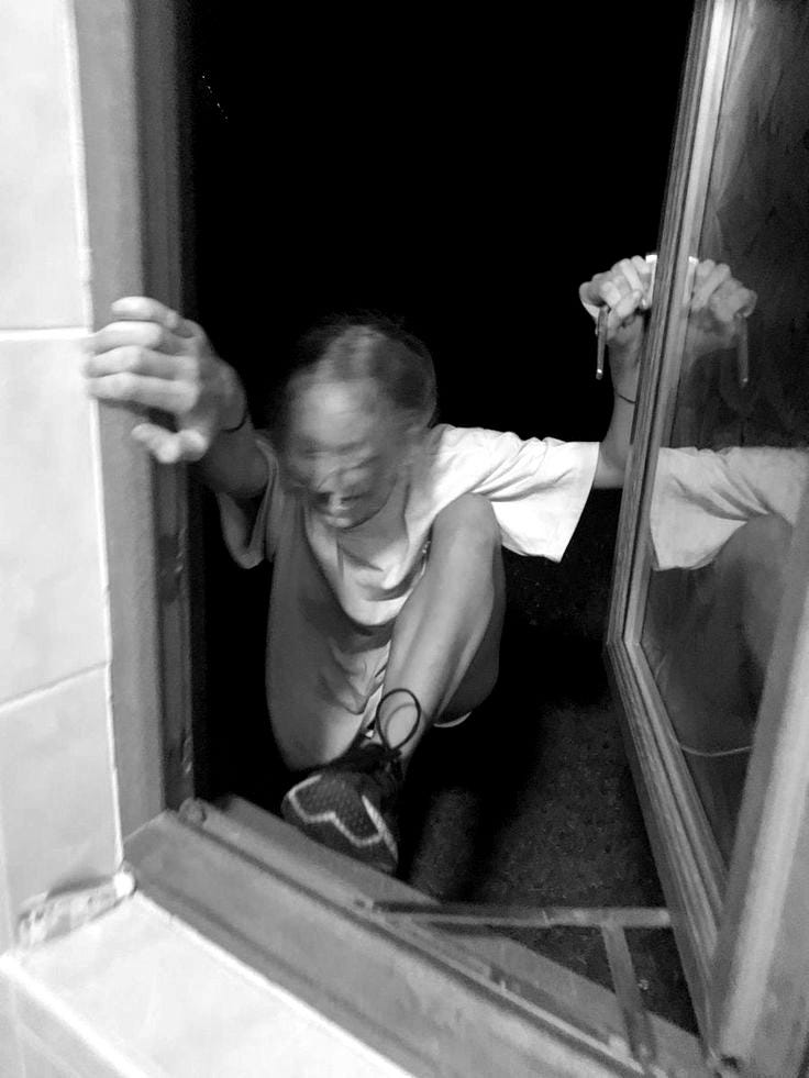 This may contain: a man in white shirt and black shoes looking through window with hand on door handle