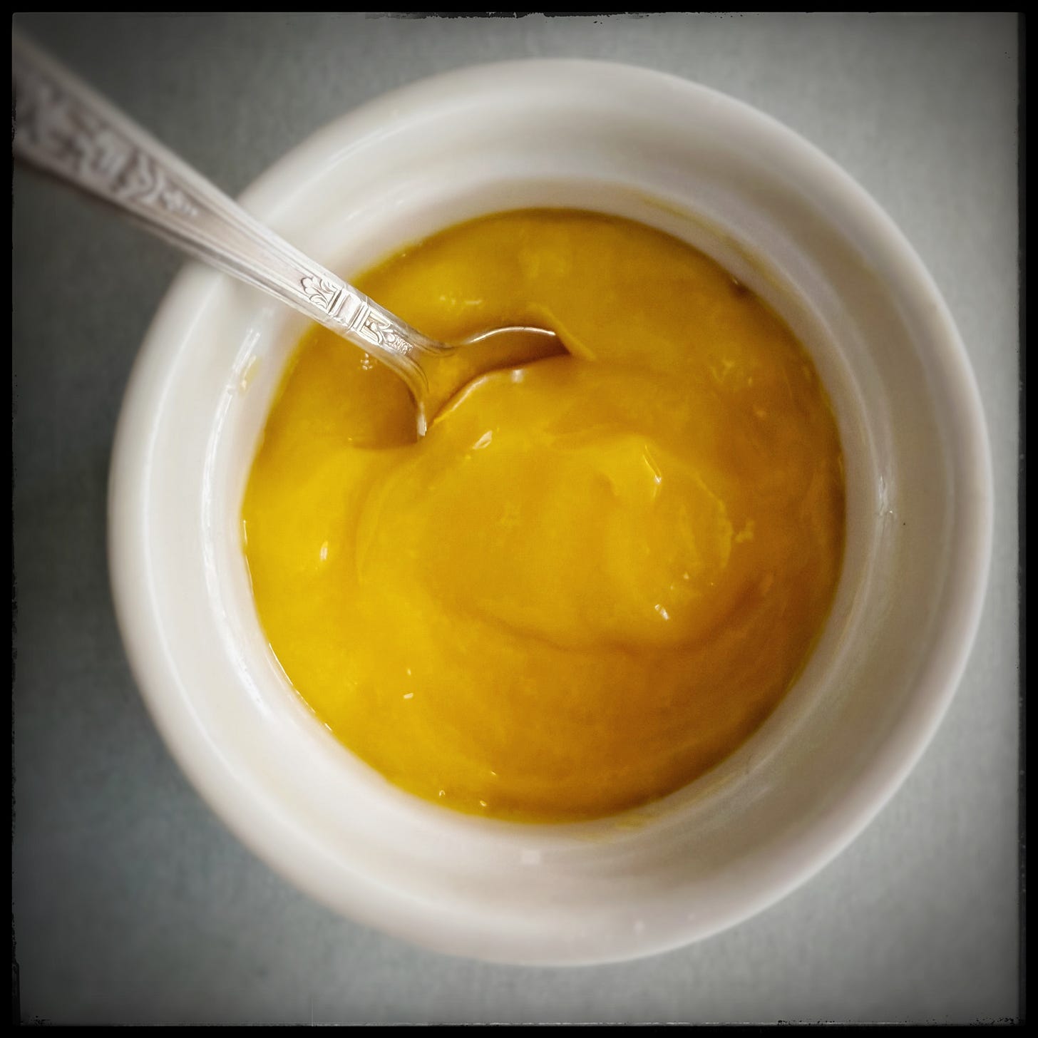 A white ceramic ramekin filled with vibrant lemon curd. 