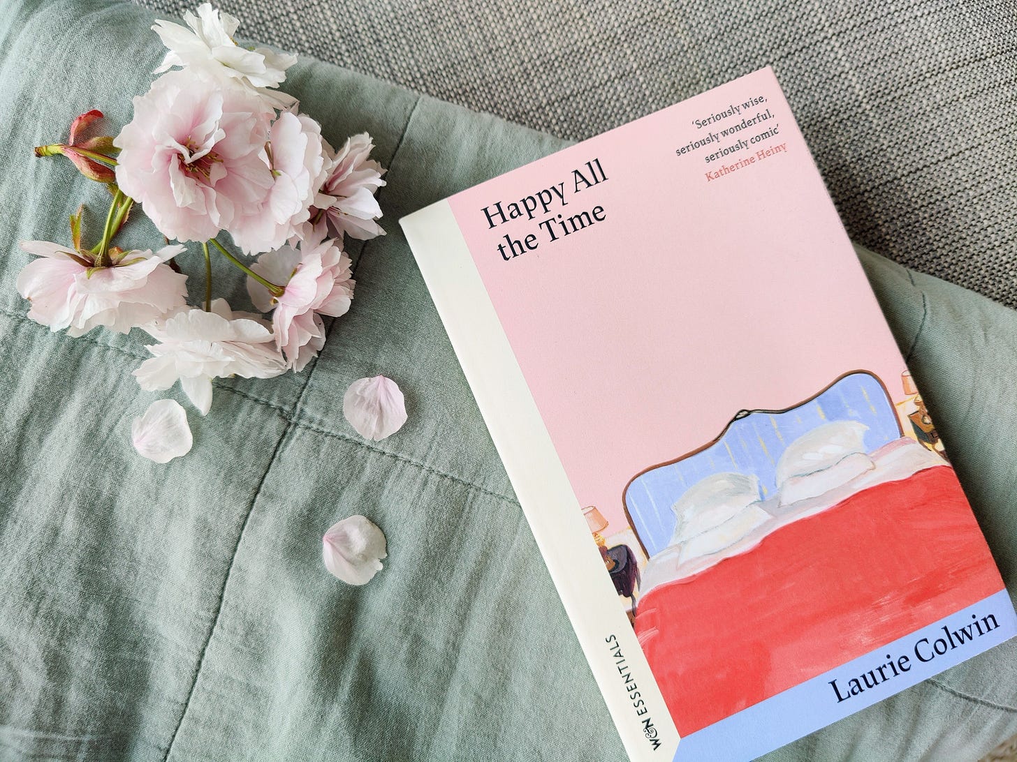 Paperback of Happy All the Time by Laurie Colwin with spring blossom petals