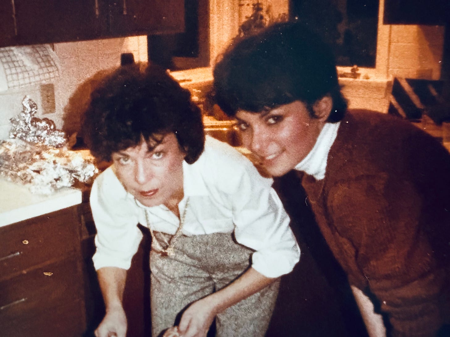 two women looking up at camera while taking something from the oven