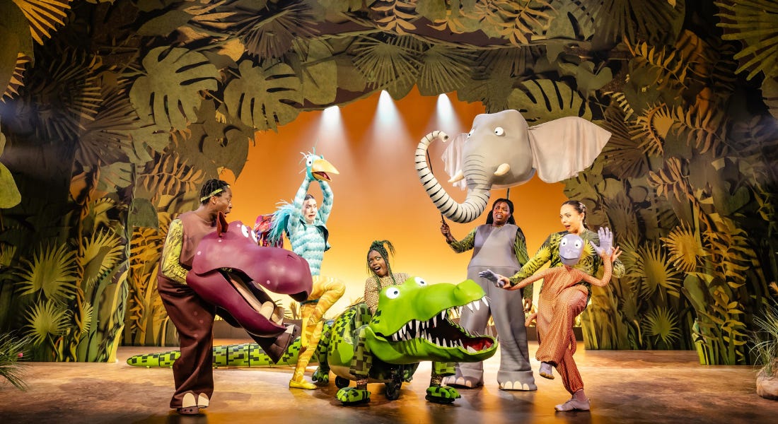 A group of animal puppet actors on stage with a leafy background behind them