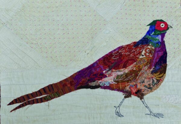 A detail image of a quilted pheasant in bright colors against a plain white patterned background with light pink dots.
