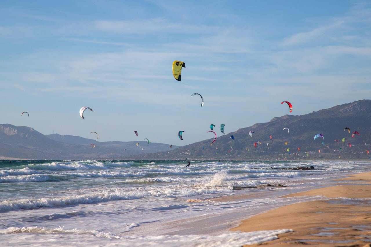 Hundreds of kitesurfers and colorful kites filling the sky above the beach in Tarifa, Spain, with mountains in the background Hundreds of kitesurfers and colorful kites filling the sky above the beach in Tarifa, Spain, with mountains in the background
