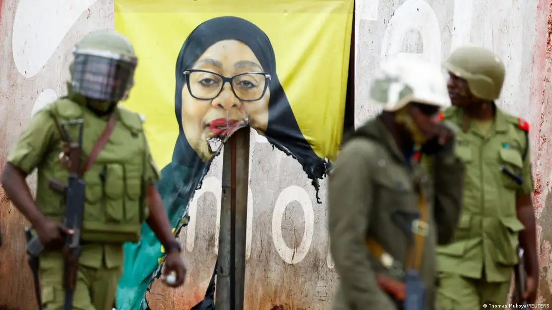 Police standing next to a destroyed campaign poster of president Samia Suluhu Hassan