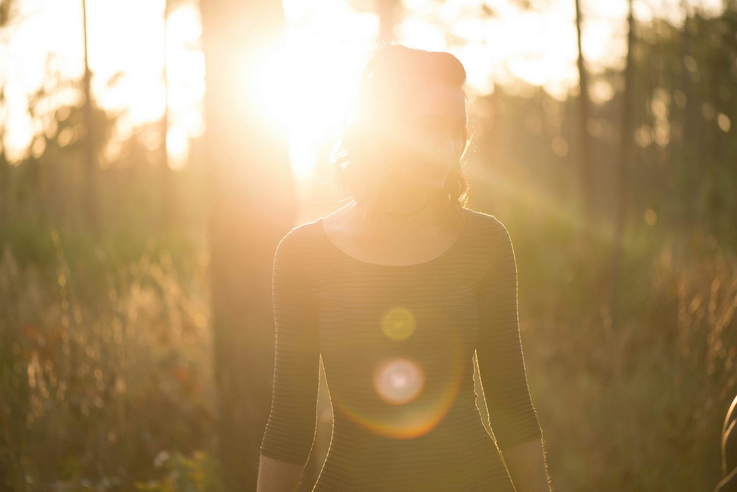 A person standing in a sunlit forest, partially obscured by bright golden light, symbolizing transformation, emergence, and self-reclamation. A person standing in a sunlit forest, partially obscured by bright golden light, symbolizing transformation, emergence, and self-reclamation.