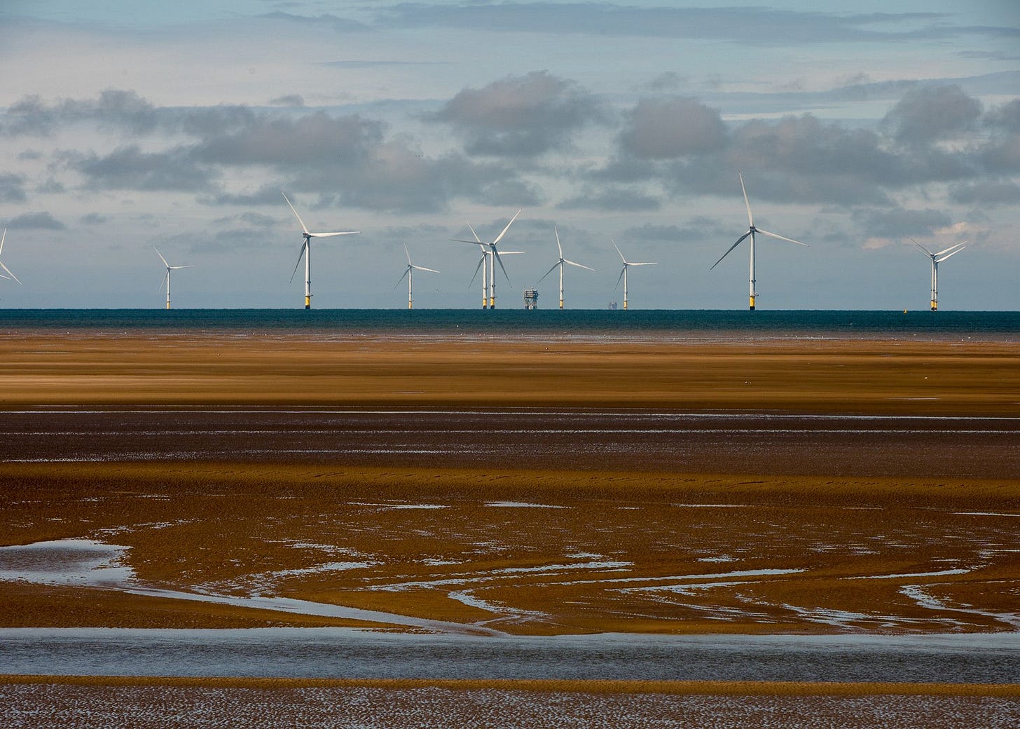 Wind turbines on the horizon with tiny rivers of water filtering through the sand below.