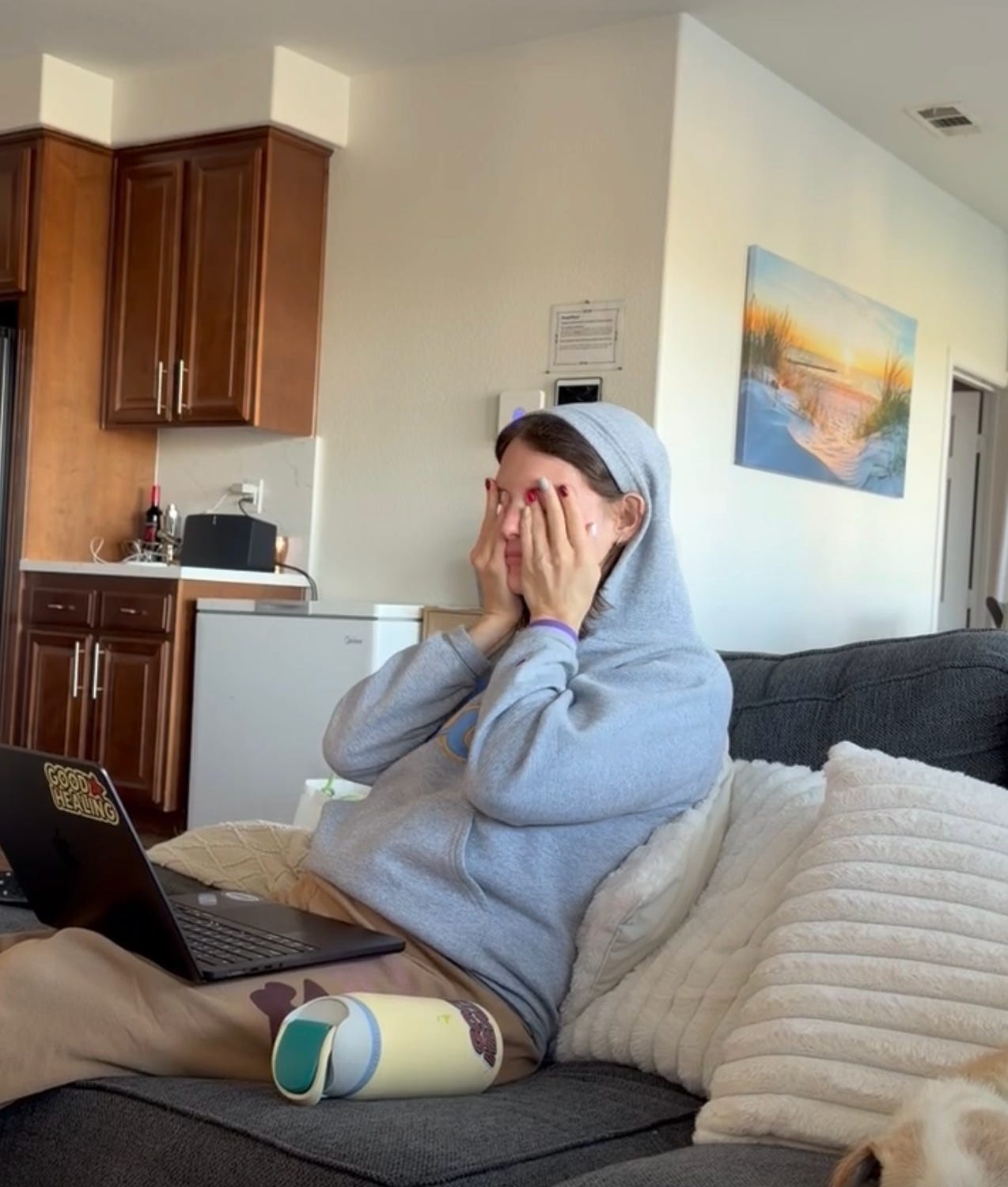 Tessa Cohen in a hoodie sitting on a couch with a laptop, covering her face in frustration during a founder work moment.
