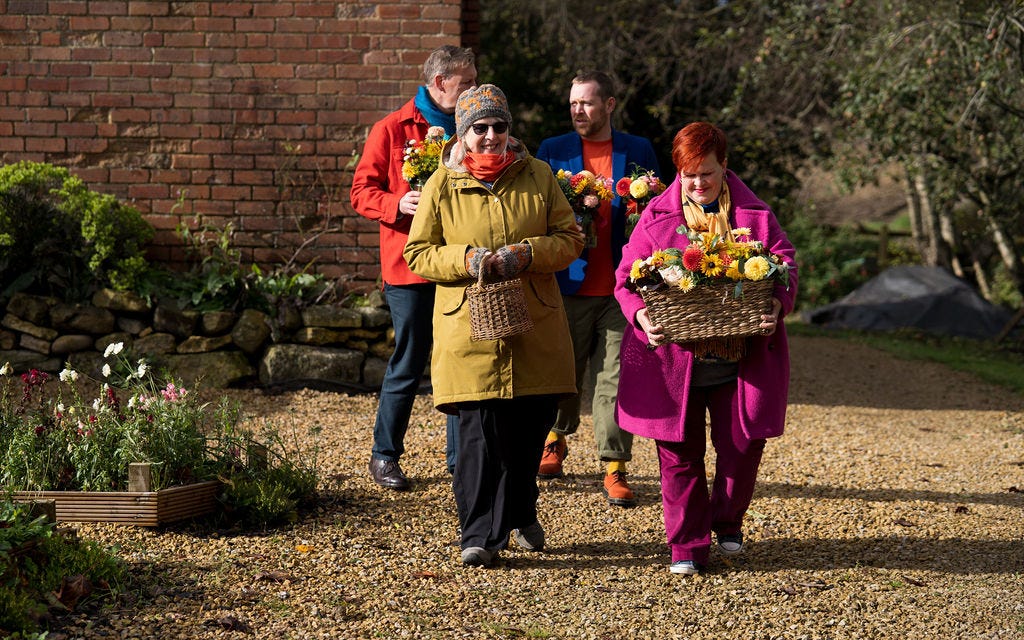 Mourners walking through the garden carrying homegrown flowers for the outdoor funeral ceremony