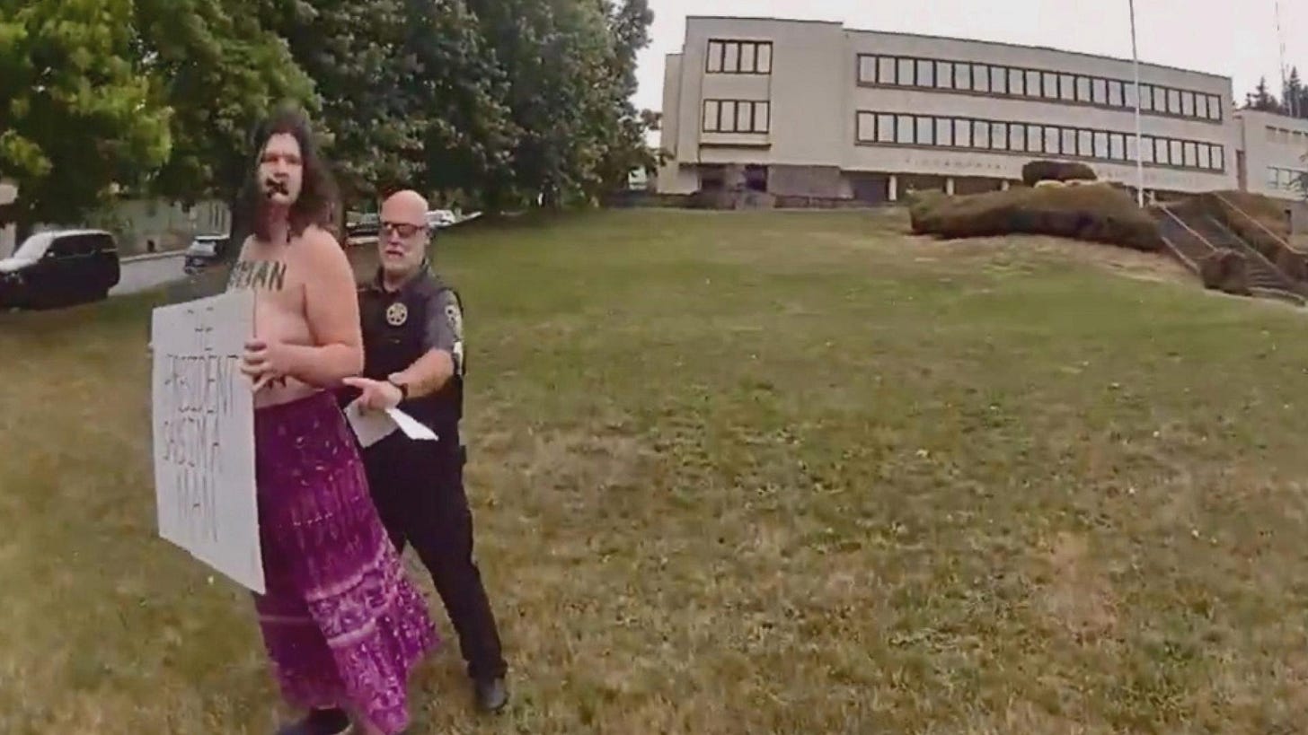 Body camera footage shows Lucy Lauser, topless and holding a protest sign, being escorted by a Skamania County Sheriff's deputy across the courthouse lawn in Stevenson, Washington.
