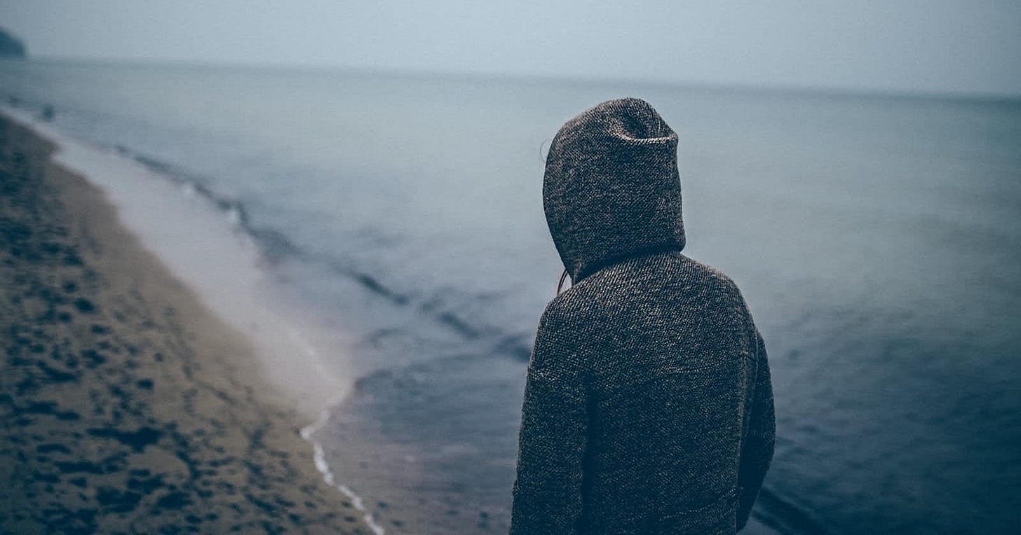Gloomy beach scene with a person in a hoodie standing by the shore, reflecting on the ups and downs of love as depicted in 'Love's Lullaby.
