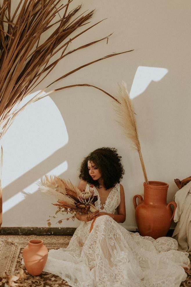 A person in a white dress sitting on the floor with a vase and dried plants

AI-generated content may be incorrect.