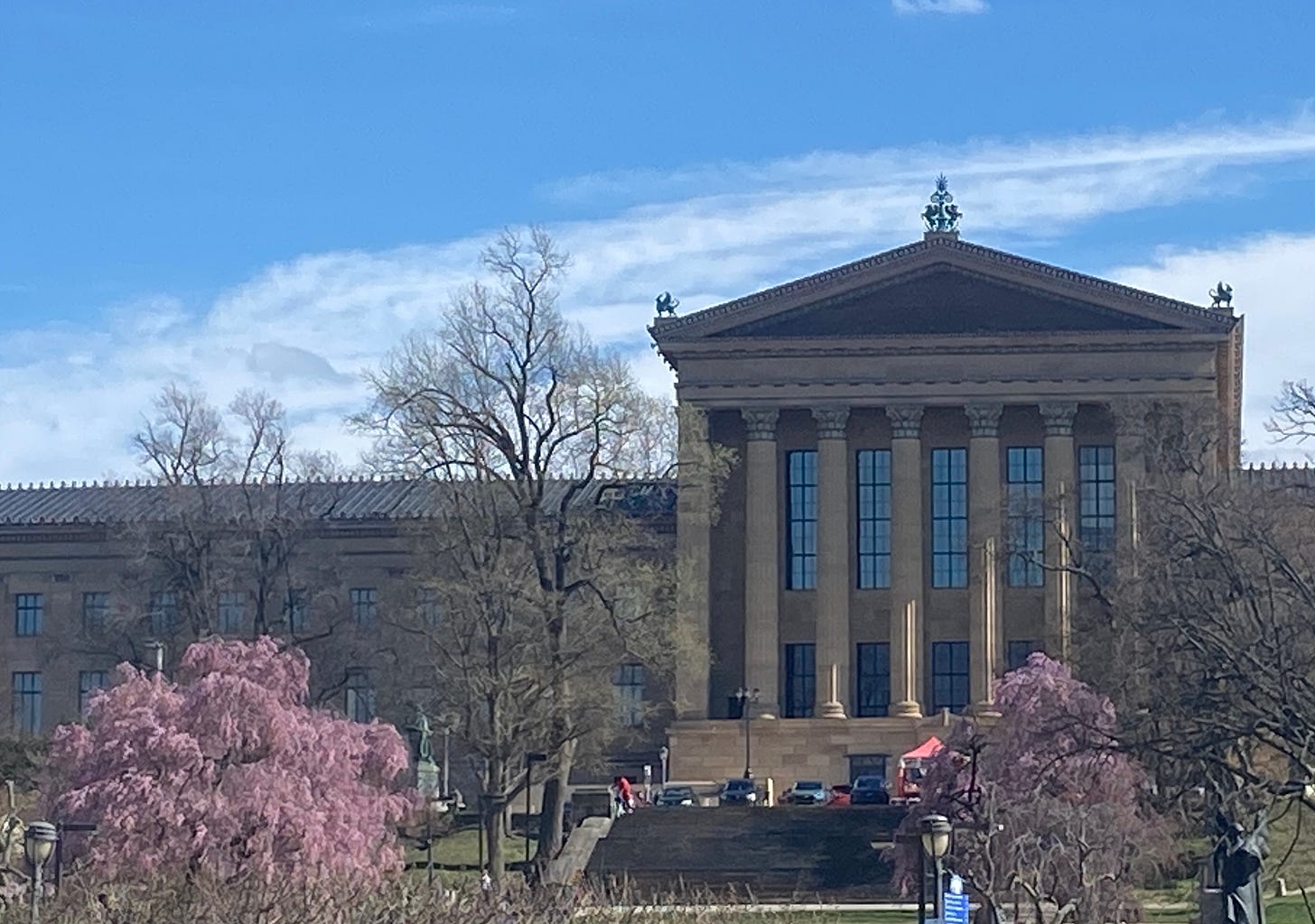 The back of the Philadelphia Ar Museum, a building with tall roman columns. In fron tof the museum are two blooming cherry tress. The back of the Philadelphia Ar Museum, a building with tall roman columns. In fron tof the museum are two blooming cherry tress.