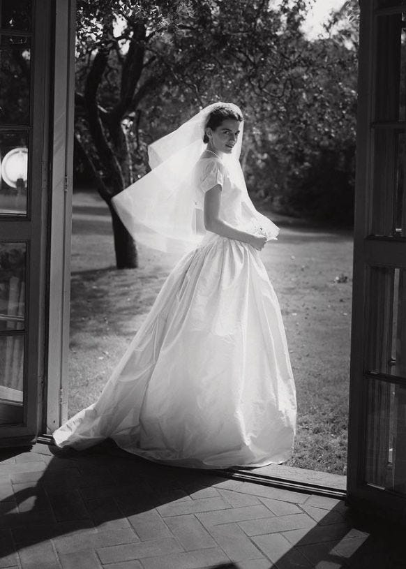 This may contain: a woman in a wedding dress is standing by an open door with her veil blowing in the wind