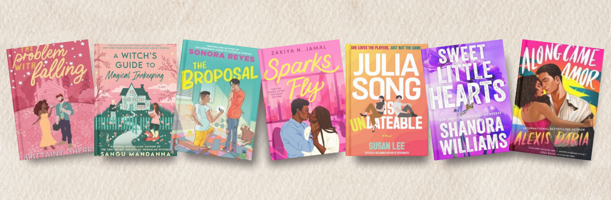 Seven illustrated romance novels arranged side by side on a neutral fabric background. The books shown are The Problem with Falling by Brittainy C. Cherry, A Witch’s Guide to Magical Innkeeping by Sangu Mandanna, The Broposal by Sonora Reyes, Sparks Fly by Zakiya N. Jamal, Julia Song Is Undateable by Susan Lee, Sweet Little Hearts by Shanora Williams, and Along Came Amor by Alexis Daria.