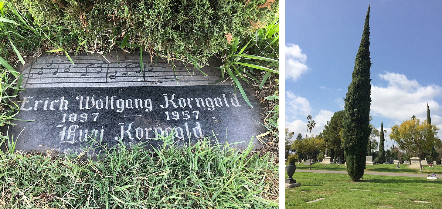 Left: Photo of a gravestone surrounded by green grass, a musical quote etched into the stone alongside "Erich Wolfgang Korngold / 1897 — 1957 / Luszi Korngold." Right: View of a large cemetery with a towering tree Left: Photo of a gravestone surrounded by green grass, a musical quote etched into the stone alongside "Erich Wolfgang Korngold / 1897 — 1957 / Luszi Korngold." Right: View of a large cemetery with a towering tree