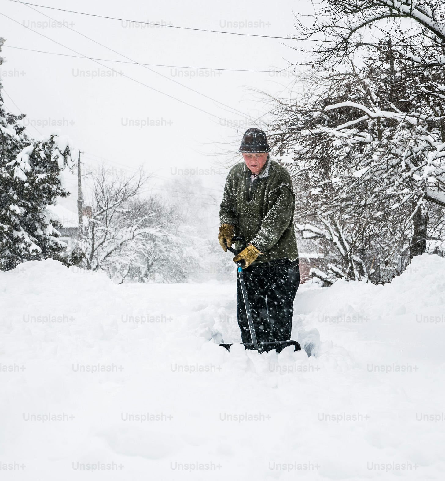 Winter snow removal. A man with a shovel clears the yard and driveway from snow during heavy snow