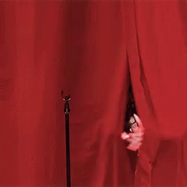 a woman in a white dress is standing in front of a red curtain . a woman in a white dress is standing in front of a red curtain .