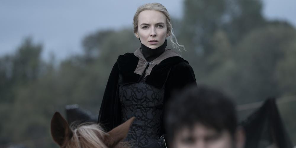 Jodie Comer in black medieval garments sitting on top of a horse looking aghast at something in the distance