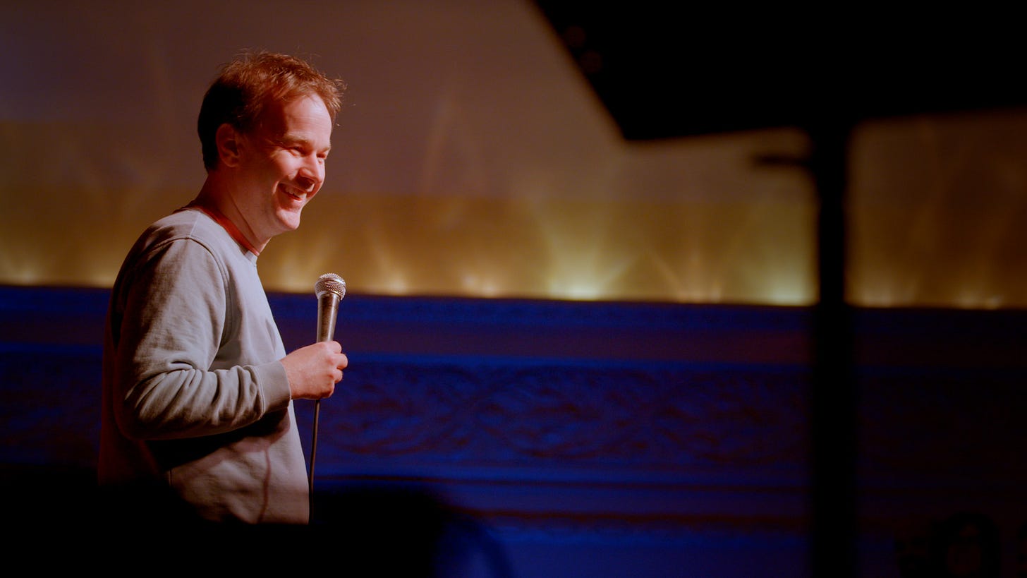 Mike Birbiglia onstage holding a microphone.