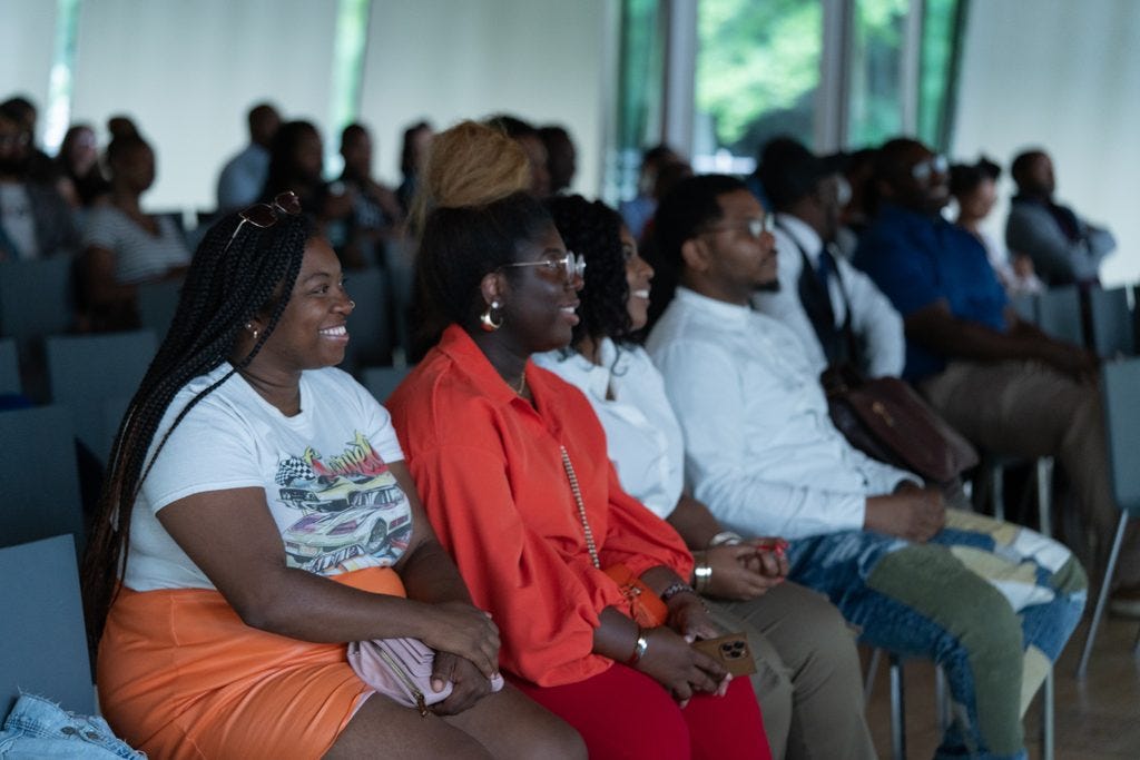 People sitting in rows attentively watching in a naturally lit room, dressed casually.