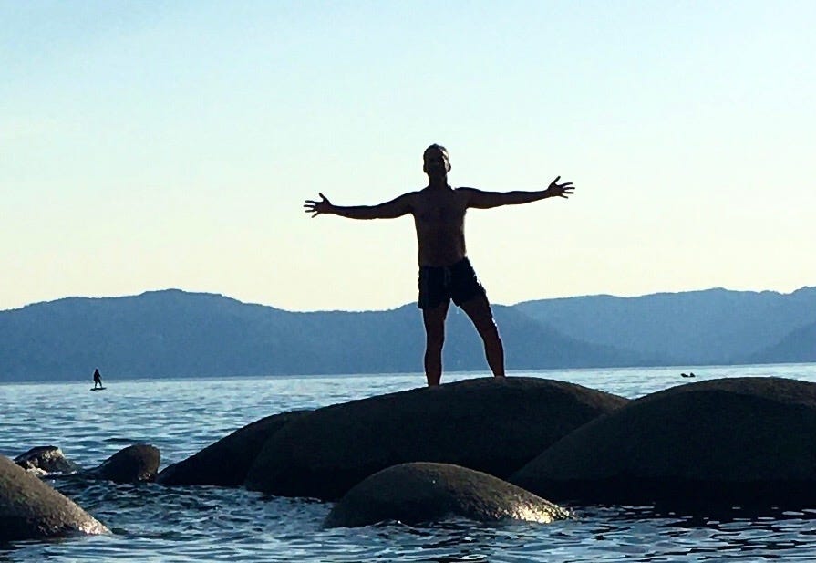 A man stands atop a giant rock near Lake Tahoe, with his arms open wide