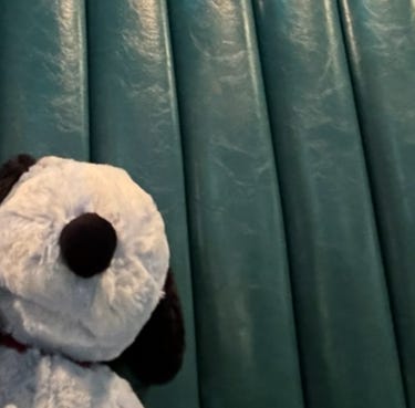 The head of a blue stuffed animal sitting in a teal restaurant booth.