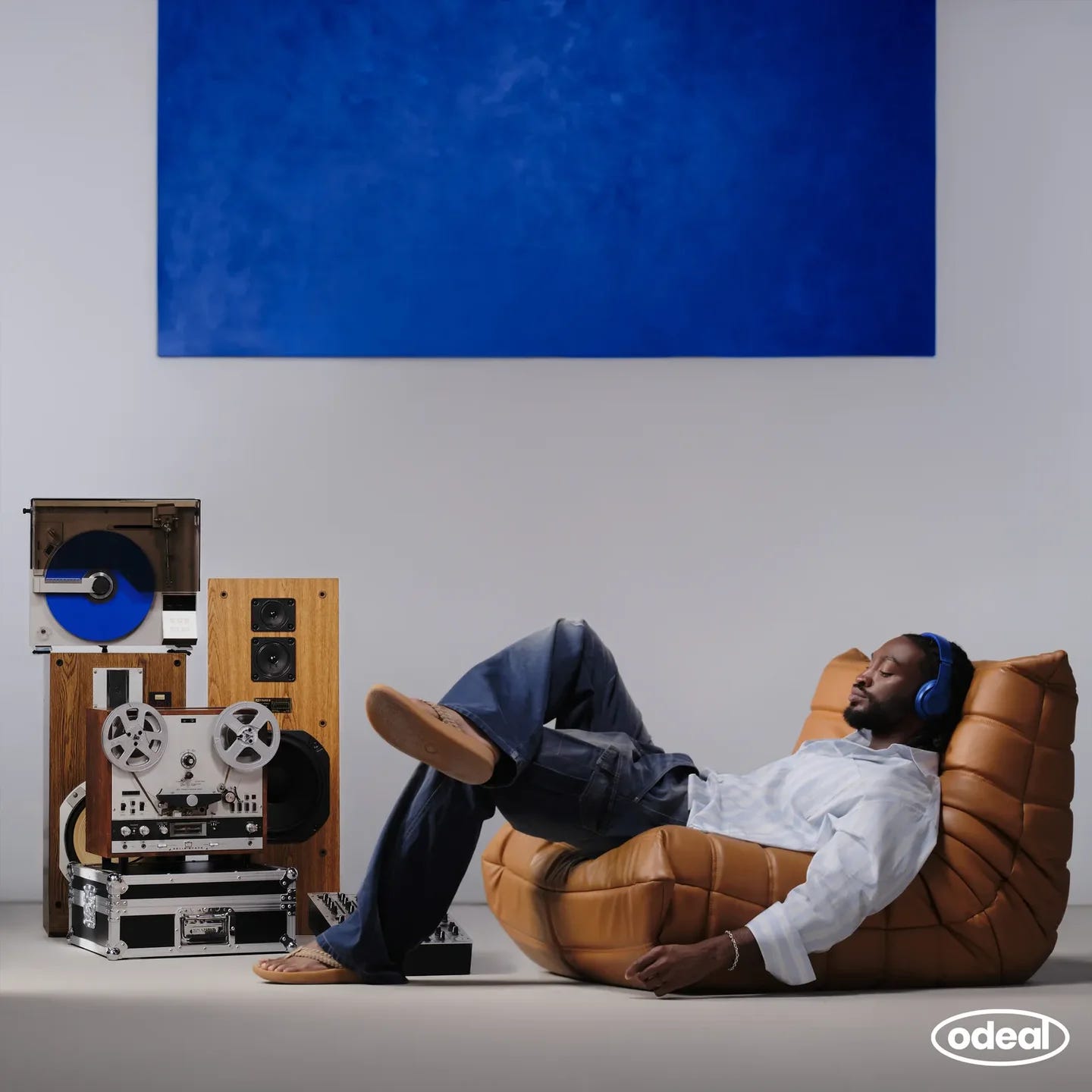 British singer Odeal sitting in a leather chair in front of a blue and gray wall near a vinyl player