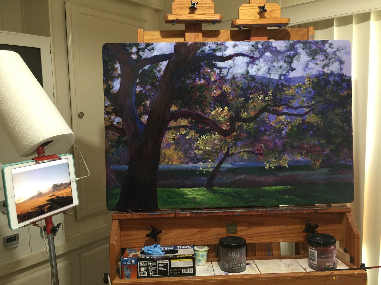 Image of a very large two column wooden easel with a landscape painting on it.