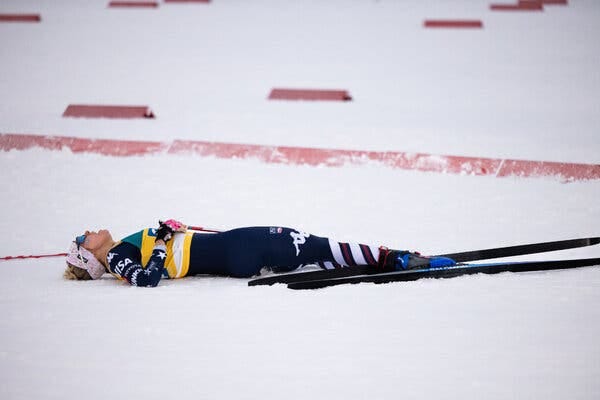 A woman wearing American stars-and-stripes ski gear lays exhausted on her back in the snow after a race looking up at the sky. A woman wearing American stars-and-stripes ski gear lays exhausted on her back in the snow after a race looking up at the sky.