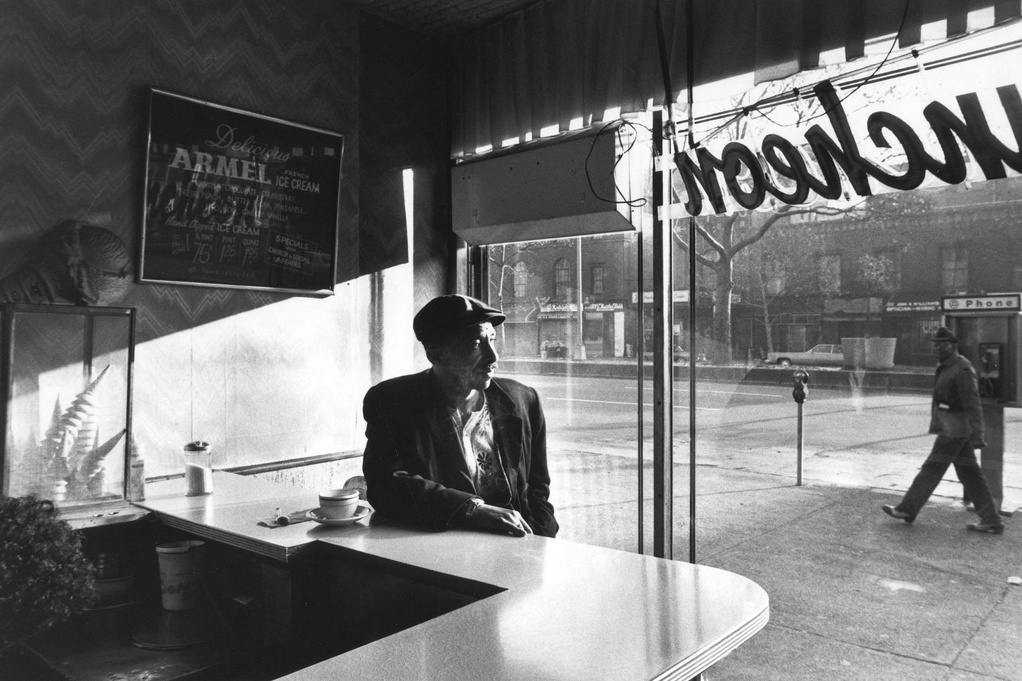 A man sitting at a restaurant counter in front of a big window looking out on the street.