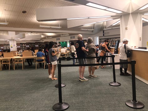 People in library borrowing books, browsing, reading 