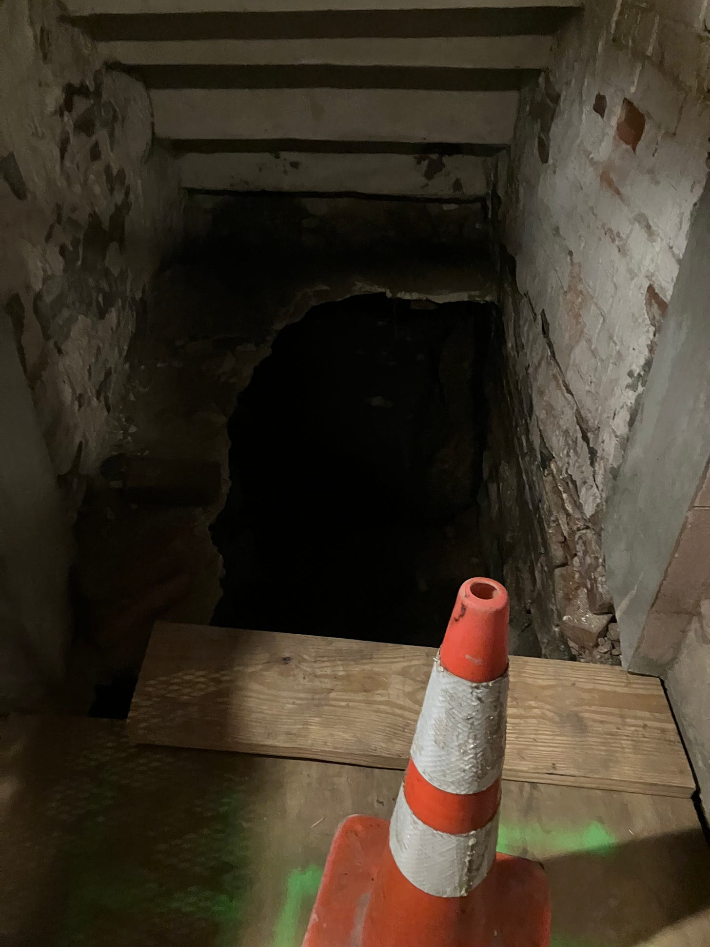 photograph of a deep hole dug under a brick-lined stoop, with a traffic cone in the foreground photograph of a deep hole dug under a brick-lined stoop, with a traffic cone in the foreground