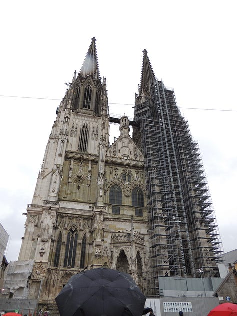 a gothic cathedral, man holding a mug of beer, a plate of sausages and bread, building by a river, a wall of cuckoo clocks, closeup of a christmas musical piece in the cuckoo shop