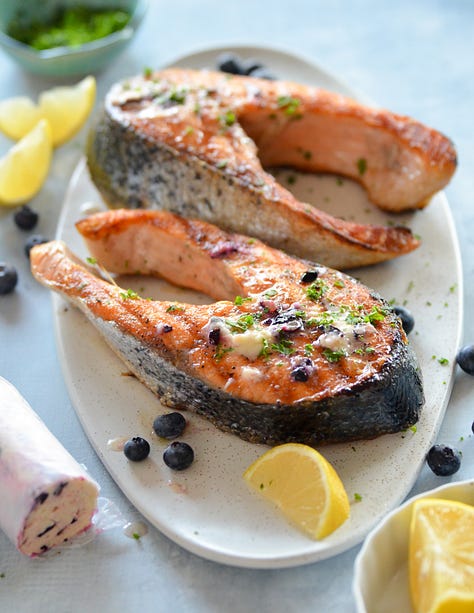 photos of fish almandine on a platter, seafood risotto in a white bowl, Karista pouring a seafood boil onto a plastic tablecloth, Karista holding a whole roasted fish, salmon with brown butter pasta with peas and mint and a crispy fish burger with special sauce sitting on a wooden board