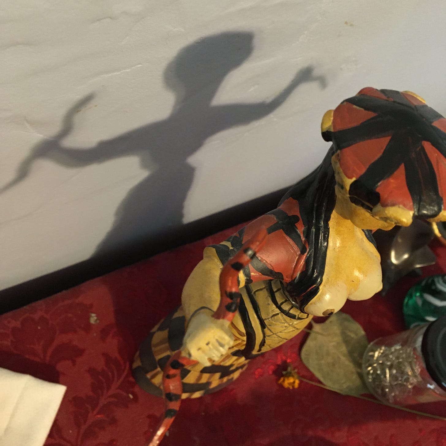 A shadow is cast on a wall by a Snake Goddess figurine standing on an altar.