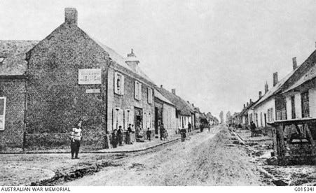Black and white photograph of an unpaved street with double storey brick houses in Pozieres, France in 1914.