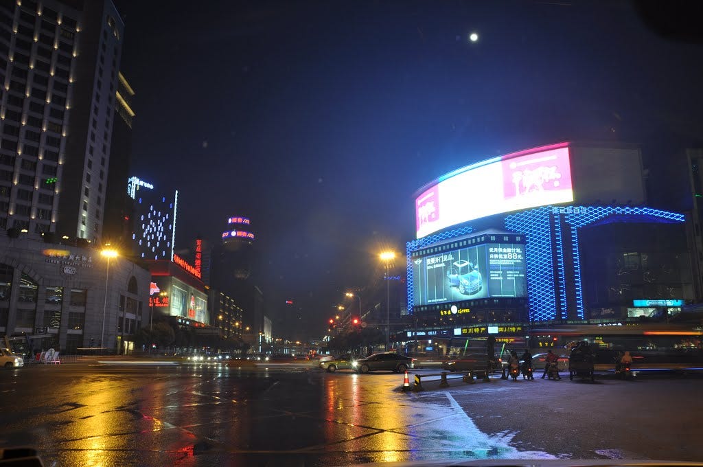A Chinese city at night lit by orange street lights under a distant moon. A Chinese city at night lit by orange street lights under a distant moon.