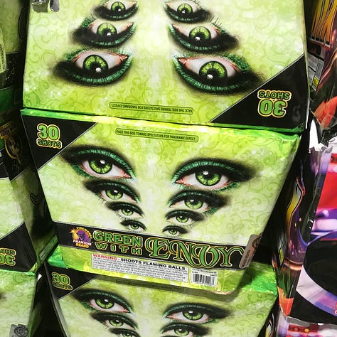 DIfferent fireworks products on the shelves at Phantom; SERENITY, POINT 'N' SHOOT, ILLIMINATI TRIANGLE, BOYZ II MEN END OF THE ROAD FINALE, a shopping cart full of fireworks, GREEN WITH ENVY, NEW WORLD ORDER, FIREY FROG, and an image of someone holding a FIREY FROG and preparing to lite fuse.