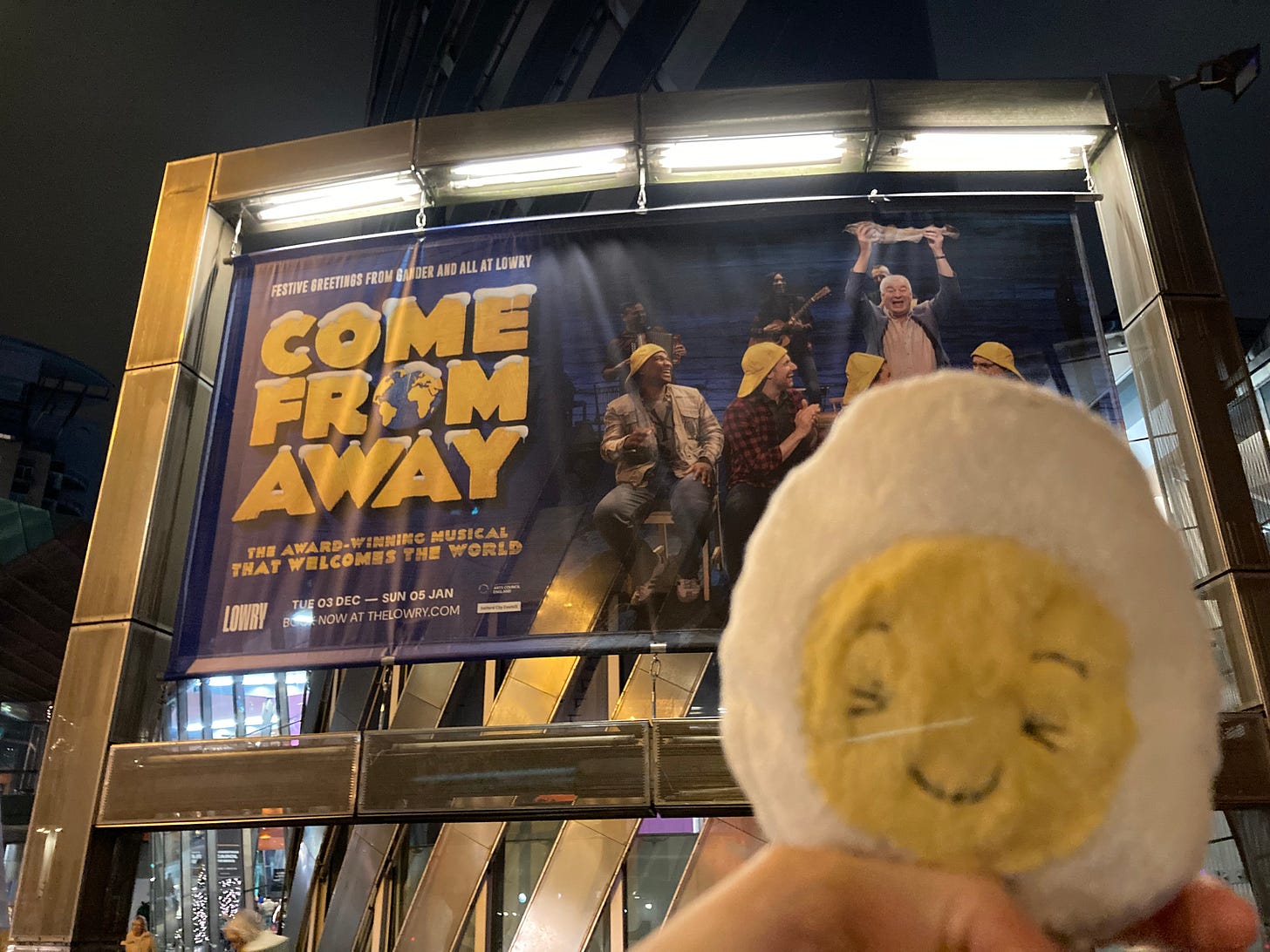 dippy the soft toy egg in front of an ourdoor banner for Come From Away the Musical. 