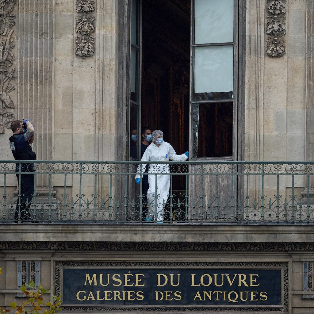 A person in a white protective suit and blue gloves stands on an ornate balcony at the Louvre Museum, looking out of an open window.