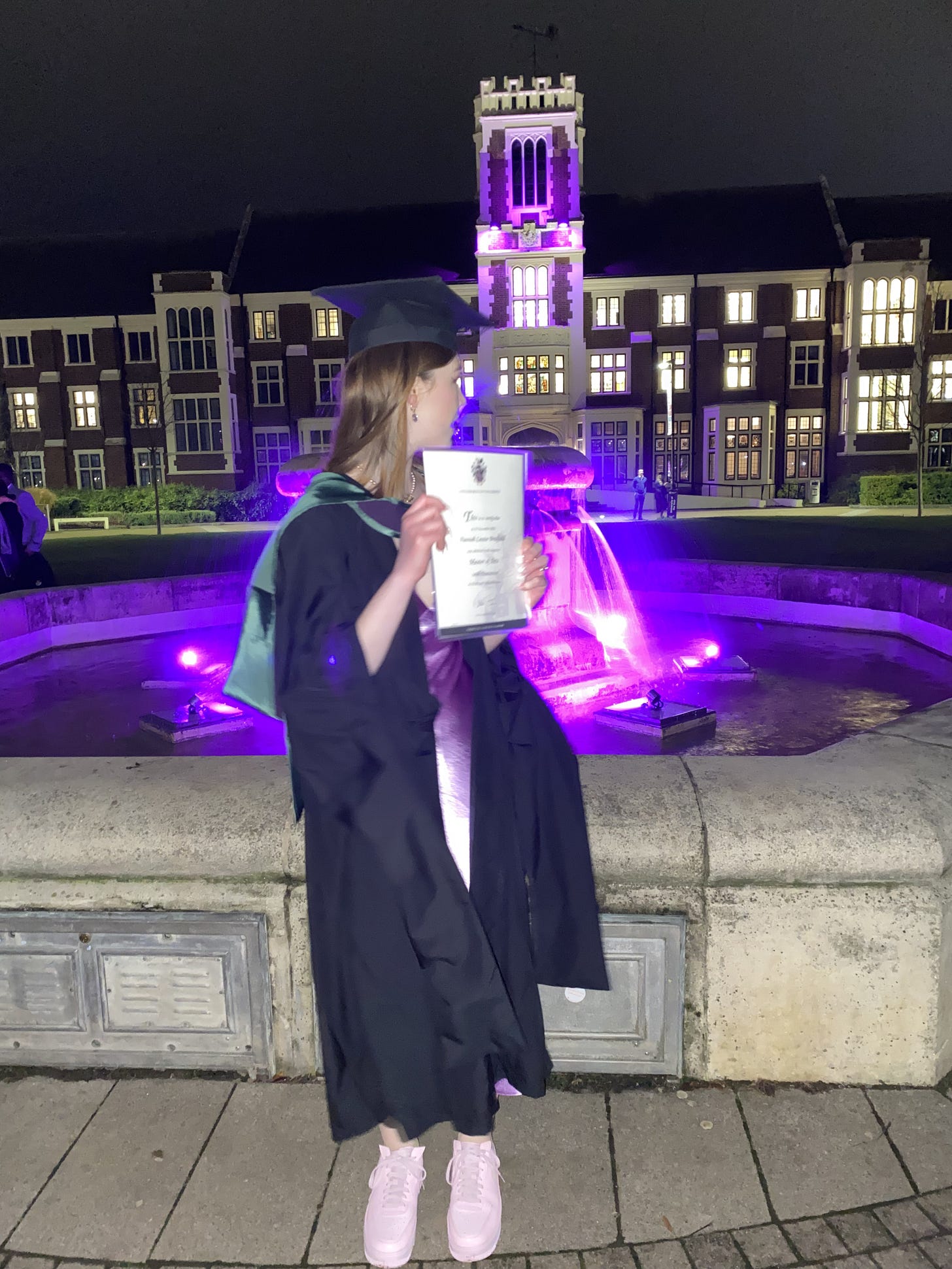 Me in a graduation cap and gown, lilac satin dress, pink trainers, holding my graduation certificate looking at the backdrop behind me, which includes a grand set of buildings with a turret in the middle. Me in a graduation cap and gown, lilac satin dress, pink trainers, holding my graduation certificate looking at the backdrop behind me, which includes a grand set of buildings with a turret in the middle.