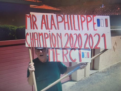 Image of a chateau on a mountain, a fan with an Alaphillippe sign, a fan wearing a t-rex costume
