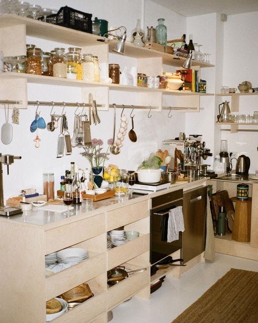 This may contain: a kitchen filled with lots of clutter and cooking utensils on wooden shelves